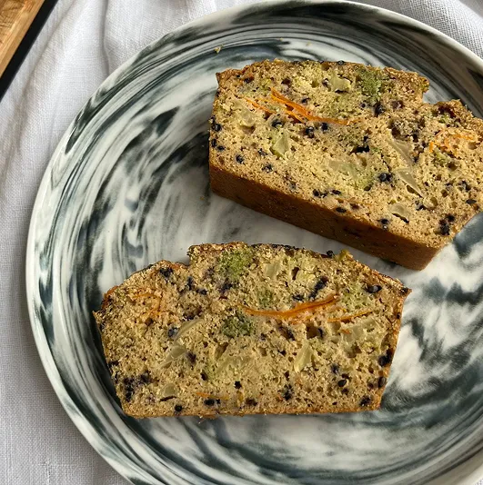Tranches de cake salé aux brocolis, carottes et graines de sésame noires, servies dans une assiette marbrée sur fond de tissu blanc