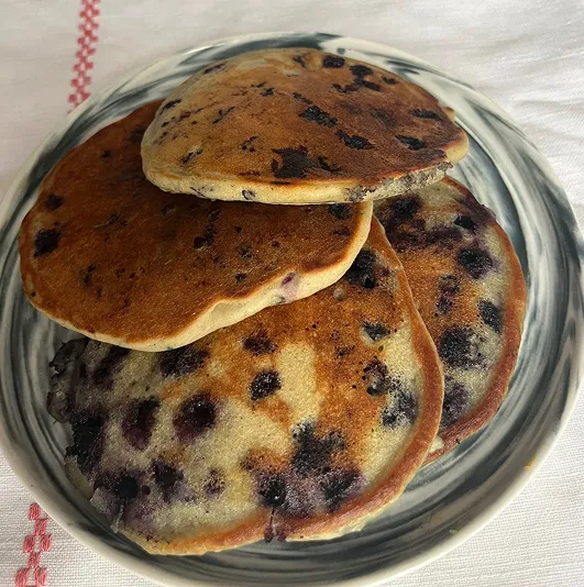 Pancakes sans gluten aux myrtilles, dorés et moelleux, empilés sur une assiette marbrée, posée sur une nappe blanche