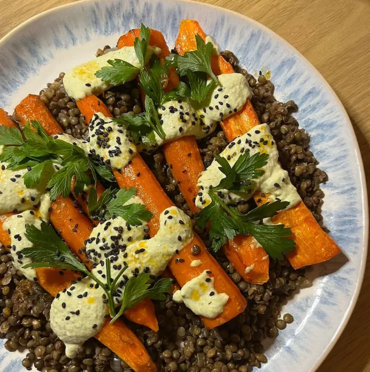 Assiette de lentilles vertes garnies de carottes rôties aux épices, sauce tahin citronnée, persil frais et graines de sésame noir, servie dans une assiette marbrée