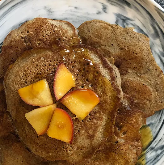 Pancakes à la pomme et à la cannelle, servis avec des quartiers de pomme fraîche et un filet de sirop d’érable, sur une assiette marbrée