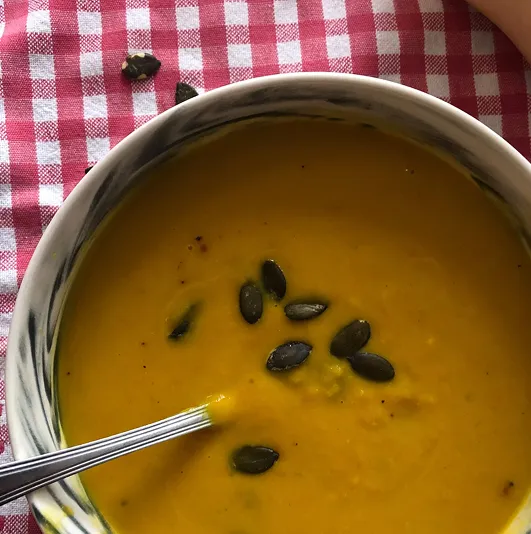 Velouté de butternut et carottes au lait de coco, servi dans un bol marbré, garni de graines de courge, sur une nappe à carreaux rouges