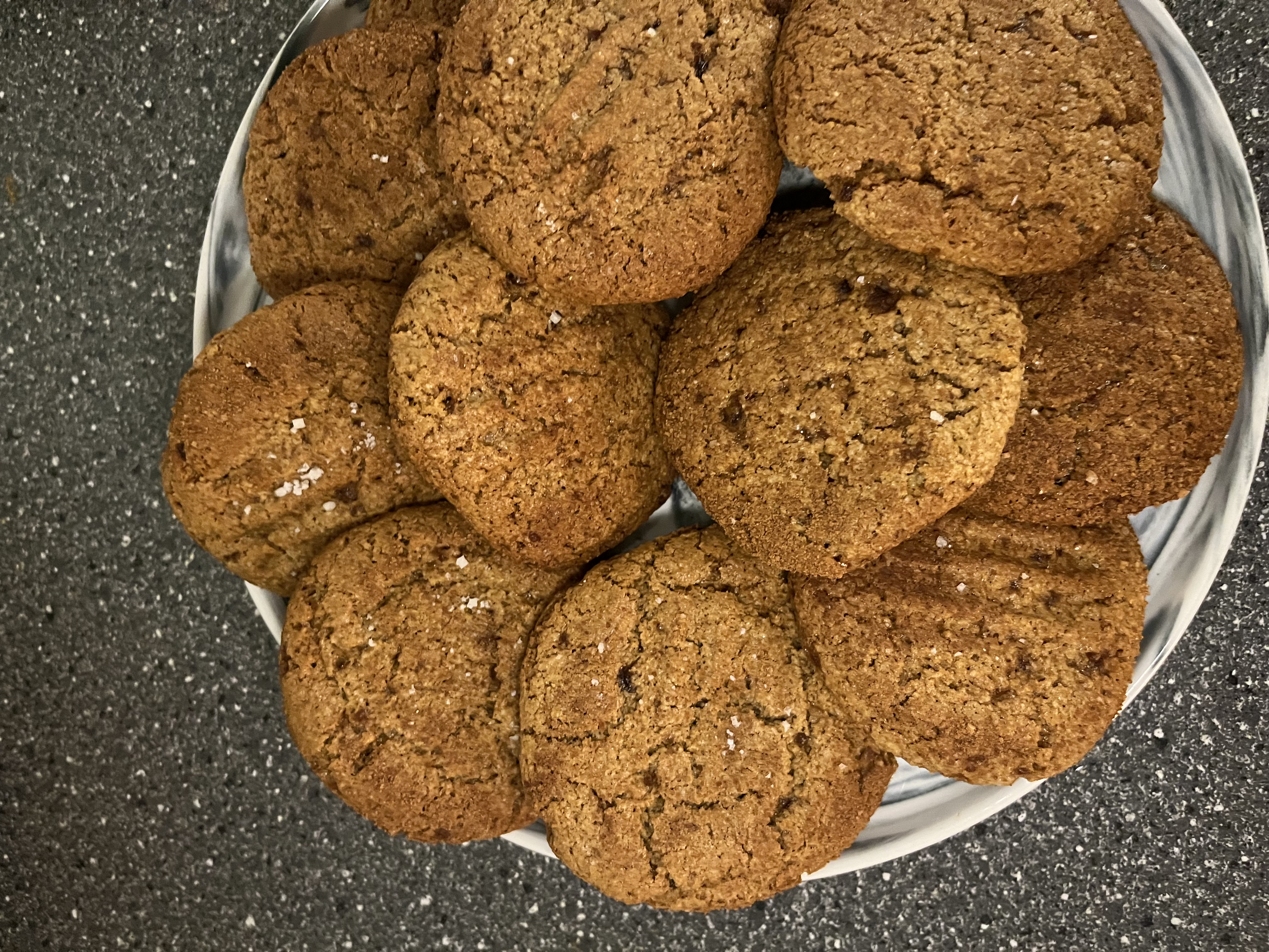 Biscuits de Noël dorés au sésame, gingembre et cannelle, légèrement saupoudrés de fleur de sel, présentés sur une assiette marbrée