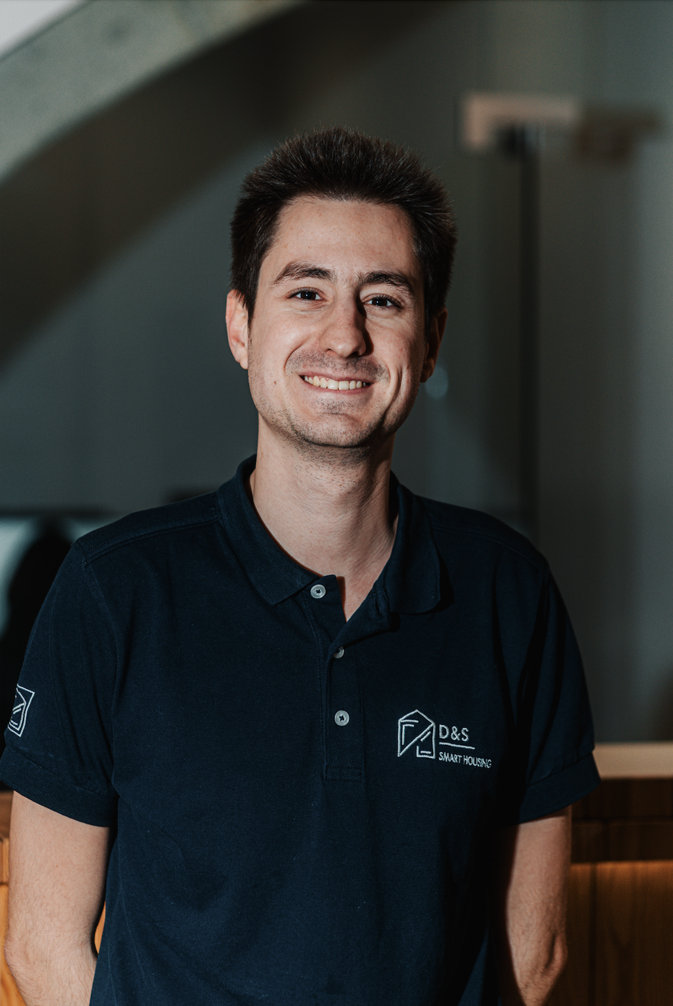 Smiling man wearing a navy blue polo shirt with D&S Smart Housing logo standing indoors.