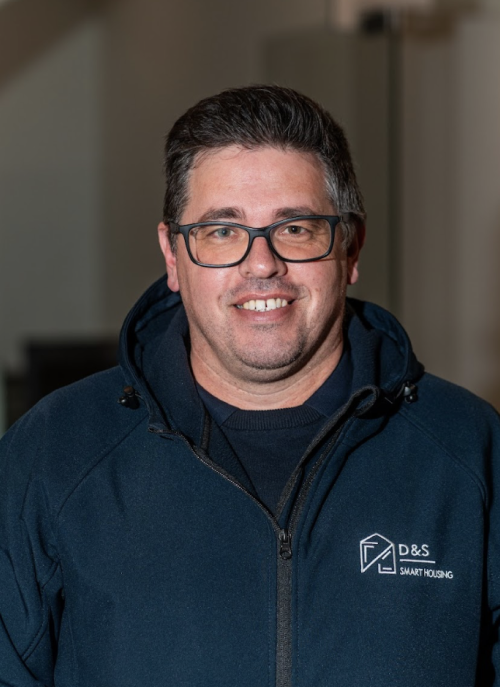 Smiling man with dark hair and beard wearing a navy blue zip-up jacket with a D&S Smart Housing logo.