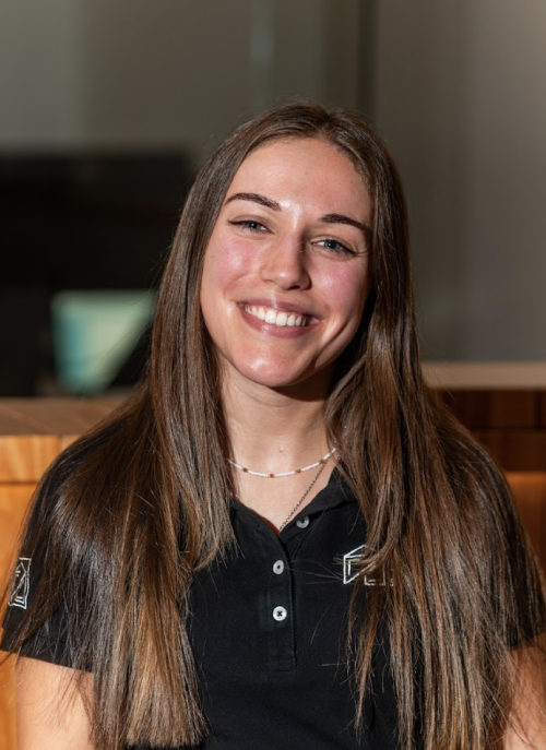 Smiling woman with long brown hair wearing a black polo shirt with D&S Smart Housing logo and a floral tattoo on her left arm.