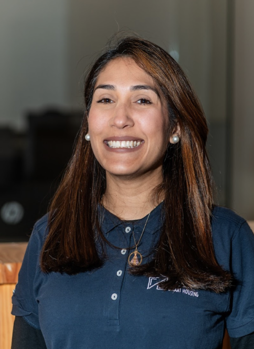 Smiling woman with long brown hair wearing a navy blue collared shirt and black long sleeves underneath.