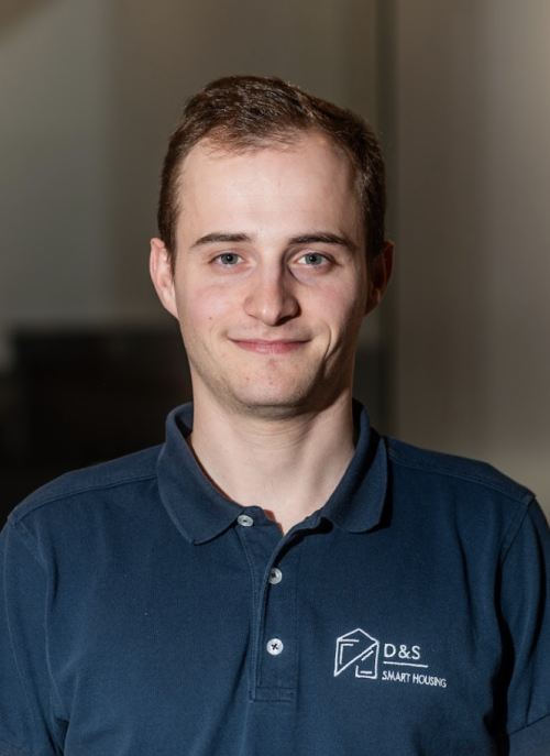 Smiling young man with short brown hair wearing a navy blue polo shirt with D&S Smart Housing logo.
