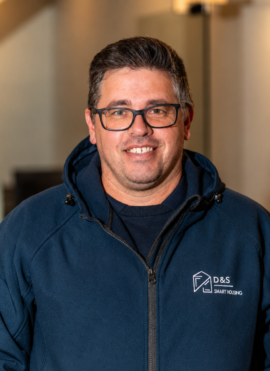 Smiling man with dark hair and beard wearing a navy blue zip-up jacket with a D&S Smart Housing logo.