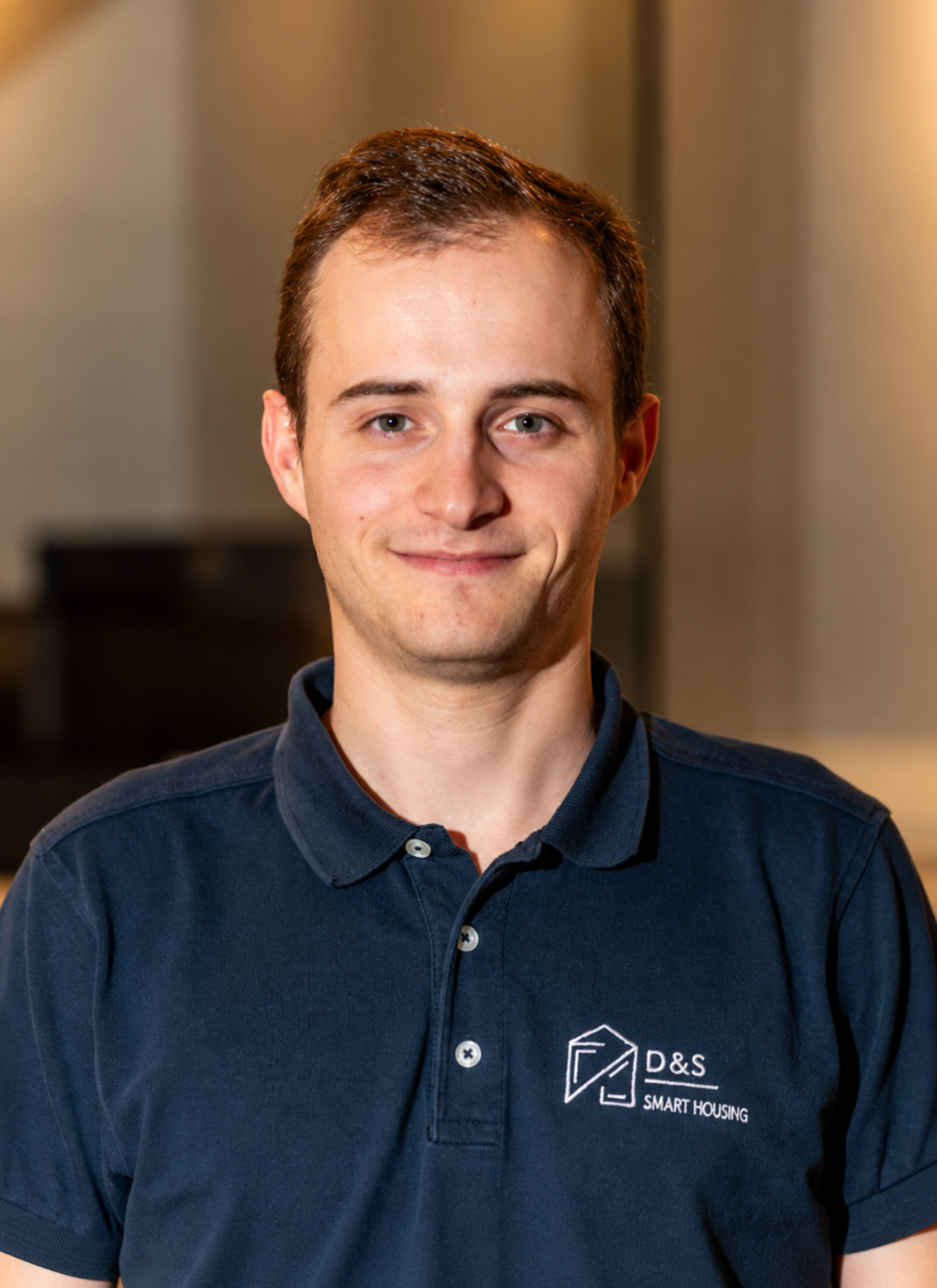 Smiling young man with short brown hair wearing a navy blue polo shirt with D&S Smart Housing logo.
