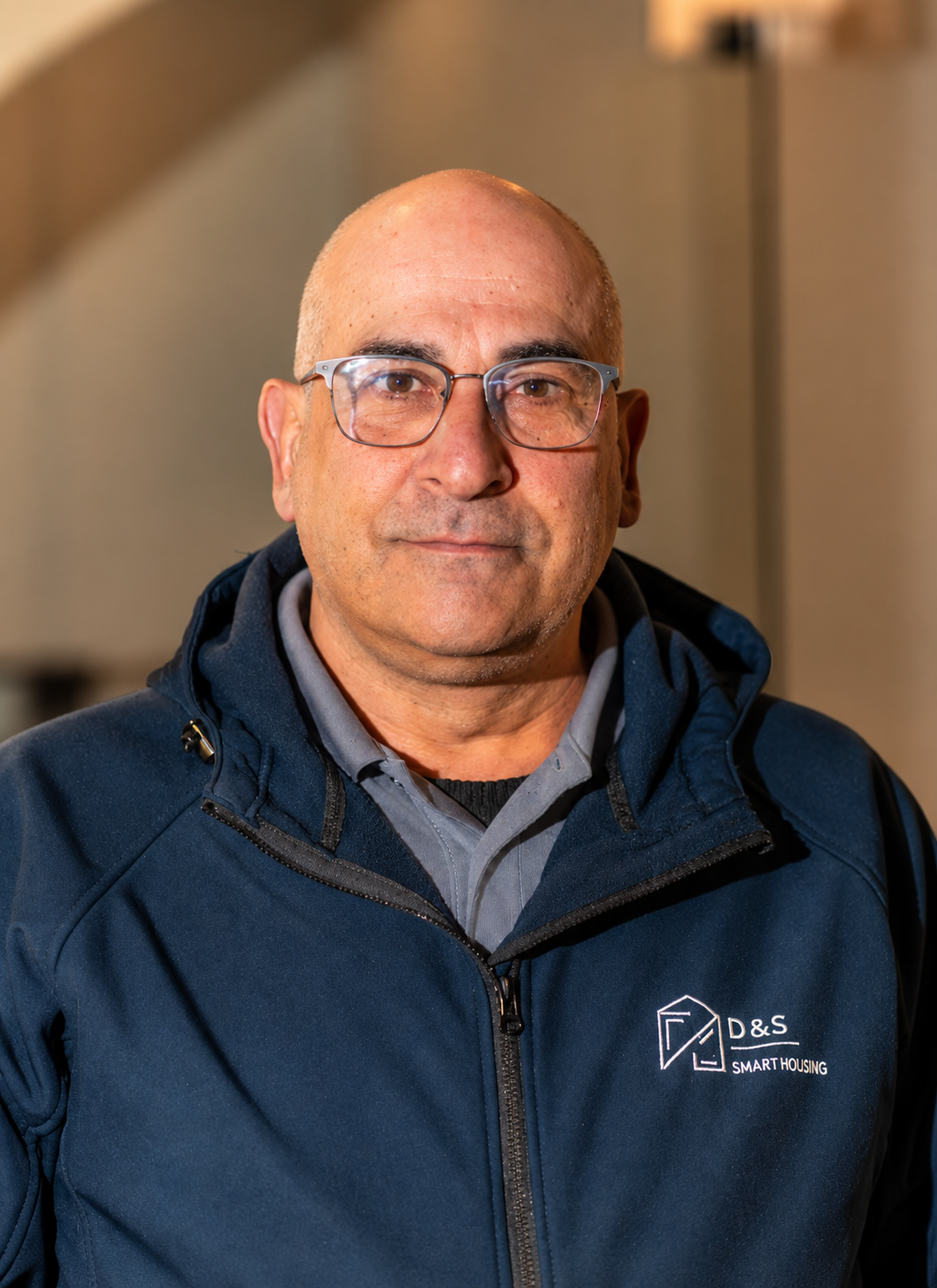 Portrait of a middle-aged man with glasses wearing a dark blue D&S Smart Housing jacket.