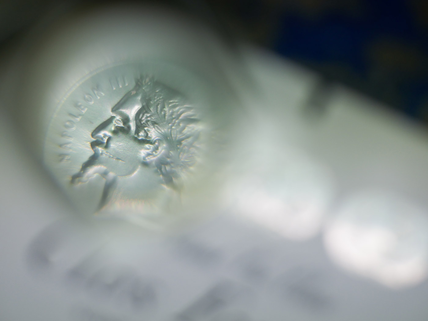 Gros plan artistique d’une pièce de monnaie à l’effigie de Napoléon III, vue à travers un effet de lentille floue.