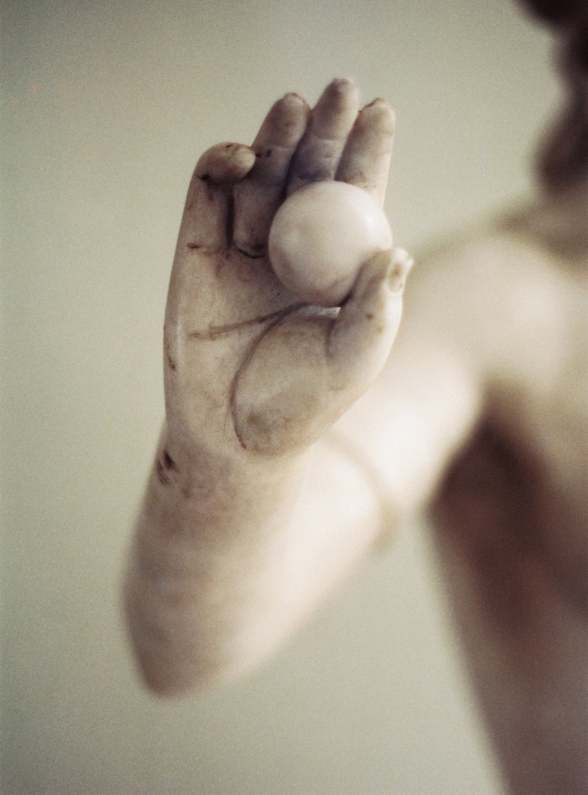 Gros plan sur une main de statue en marbre tenant une sphère, photographie artistique au rendu doux et épuré.