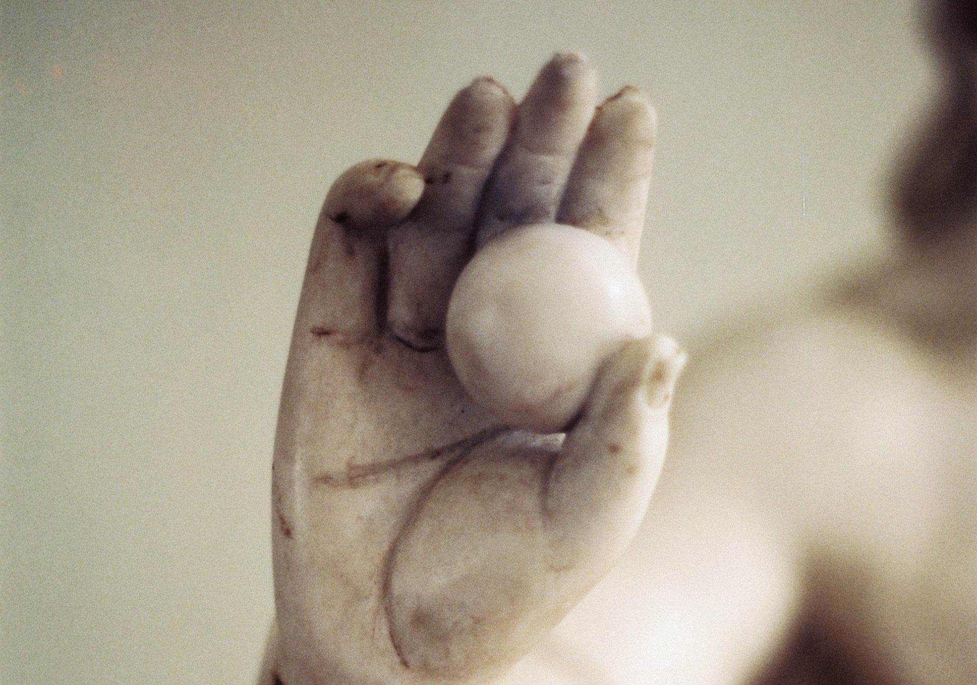 Gros plan sur une main de statue en marbre tenant une sphère, photographie artistique au rendu doux et épuré.