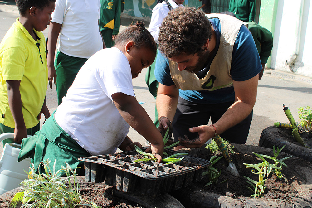 Greenpop volunteer planting seedlings with a child