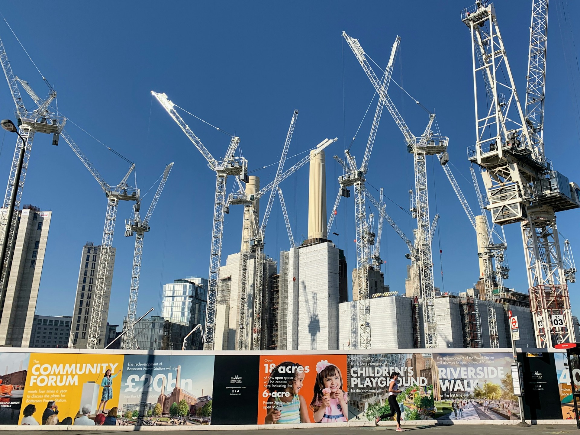 Cranes over Battersea Power Station development and hoardings showing CGI images of the development. Blue sky in background. Image credit: John Cameron