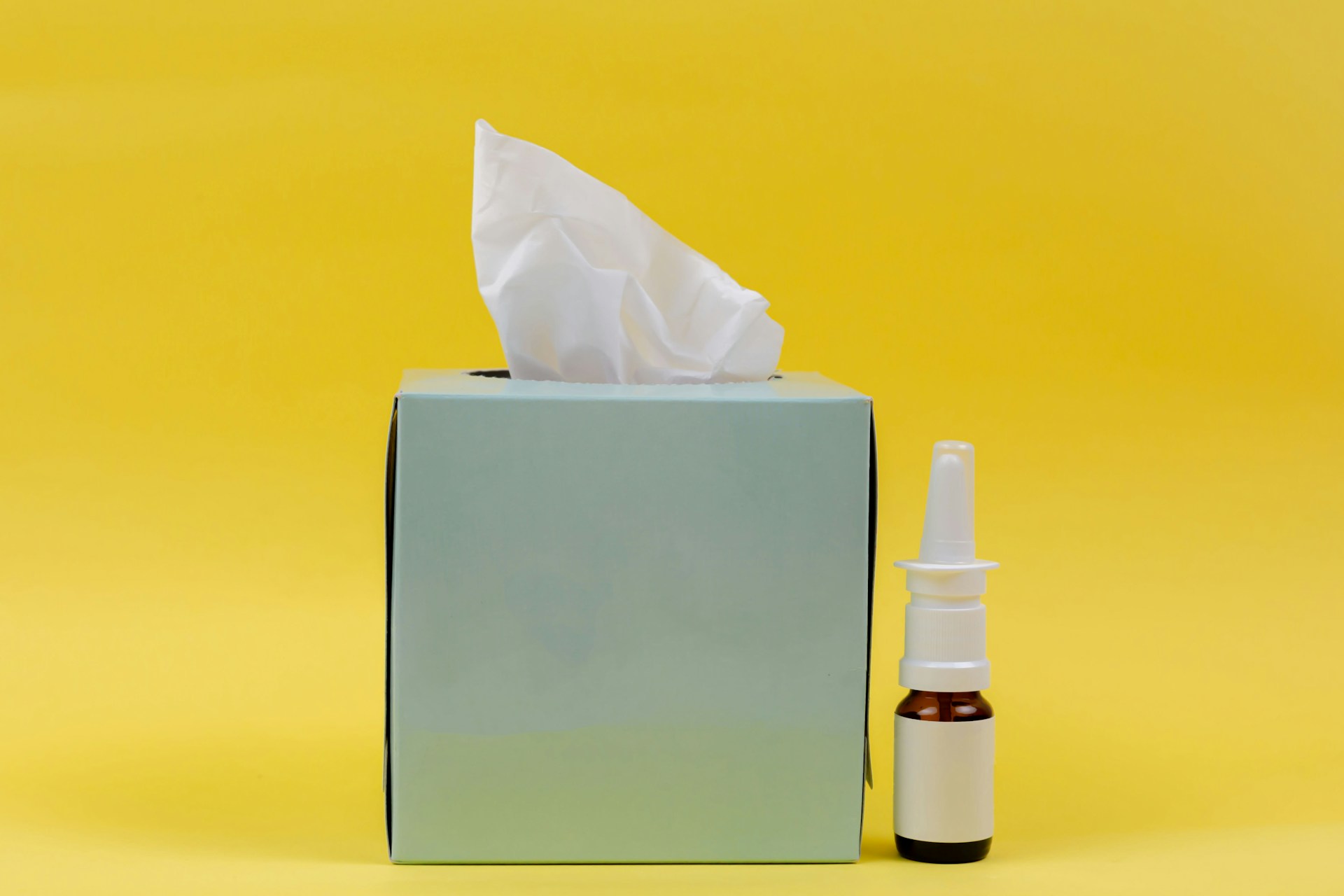 A box of tissues and a nose clearer thing on a yellow background.