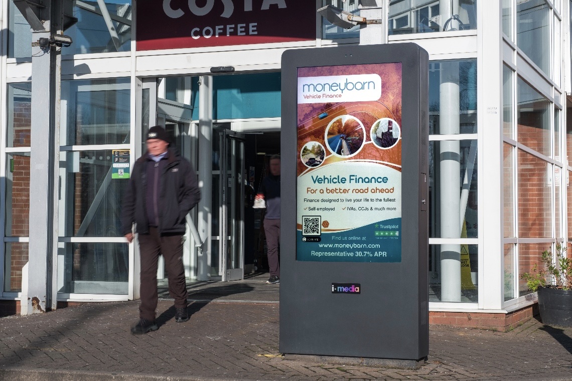 A digital screen showing a Moneybarn advertisement at motorway services