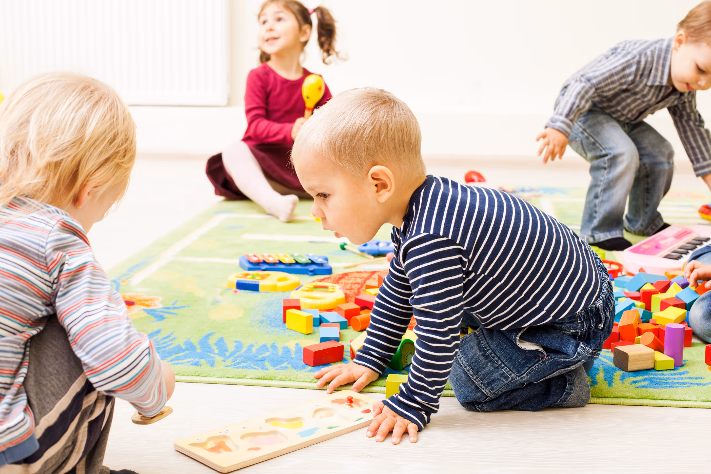 Kleine Kinder spielen auf einem Teppich mit bunten Bauklötzen und Holzpuzzles.