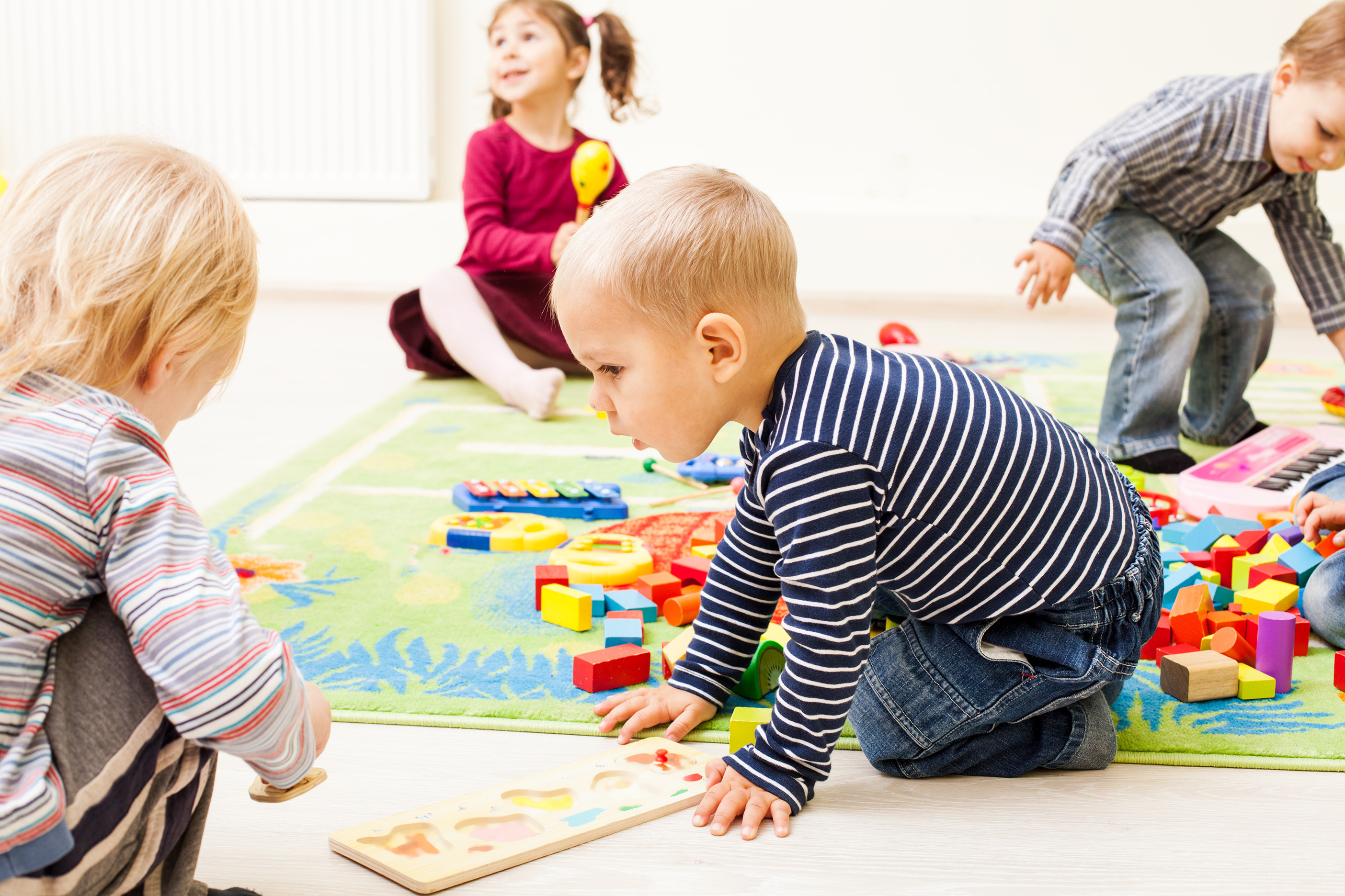 Kleine Kinder spielen auf einem Teppich mit bunten Bauklötzen und Holzpuzzles.