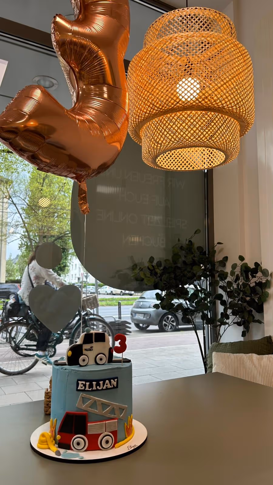 Geburtstagskuchen mit Feuerwehrauto und Polizei, Zahl 3, im Café mit goldener 3er-Ballondekoration.