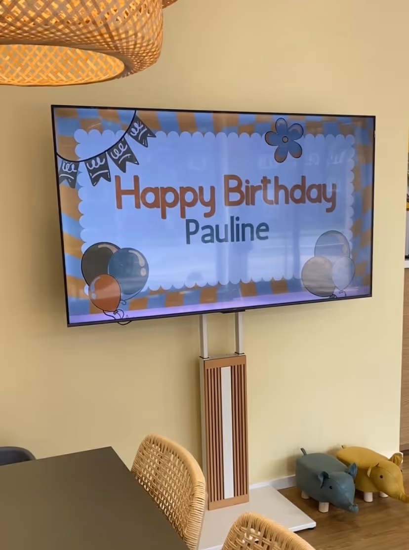 Fernseher mit Geburtstagsgruß 'Happy Birthday Pauline' in einem Raum mit Stühlen und Tierhockern.
