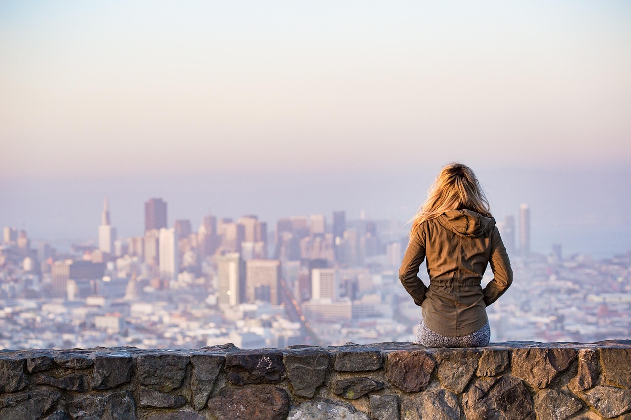 Woman sitting on wall looking at city scape