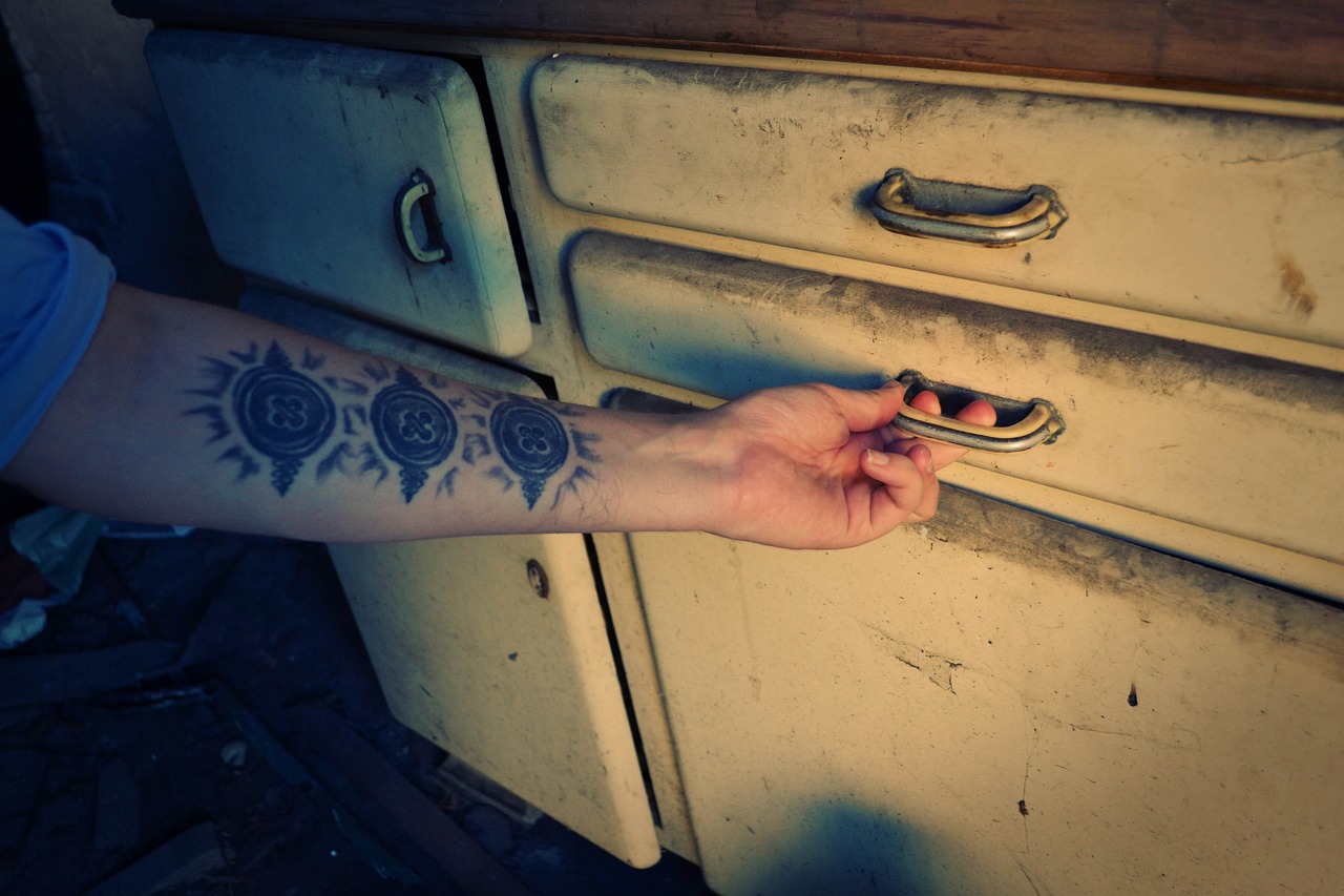 A person’s hand opening a worn kitchen drawer, with aged paint and metal handles visible