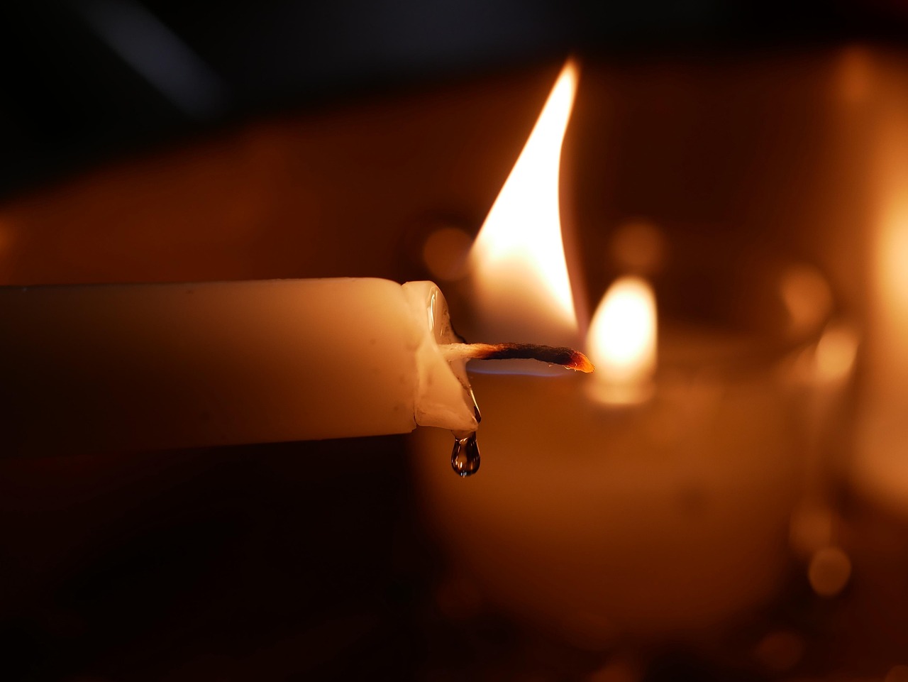 Close-up of a lit candle in a dim setting, its steady flame glowing warmly against a dark background