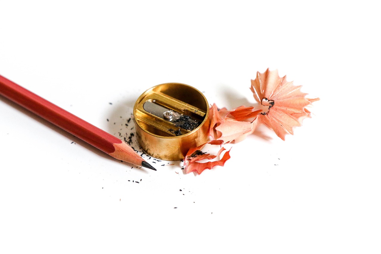 A sharpened red pencil beside a brass pencil sharpener and pencil shavings