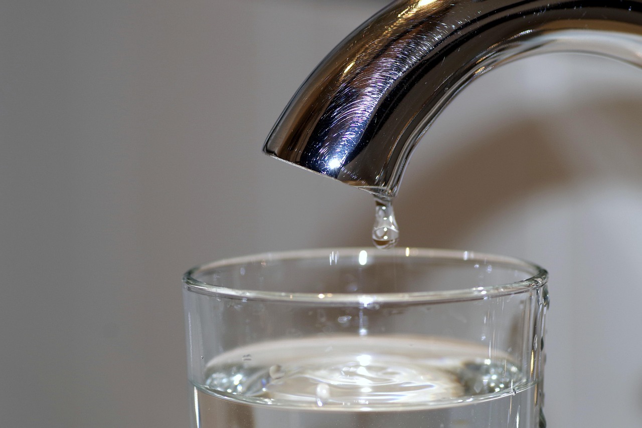 Water dripping slowly from a tap into a glass