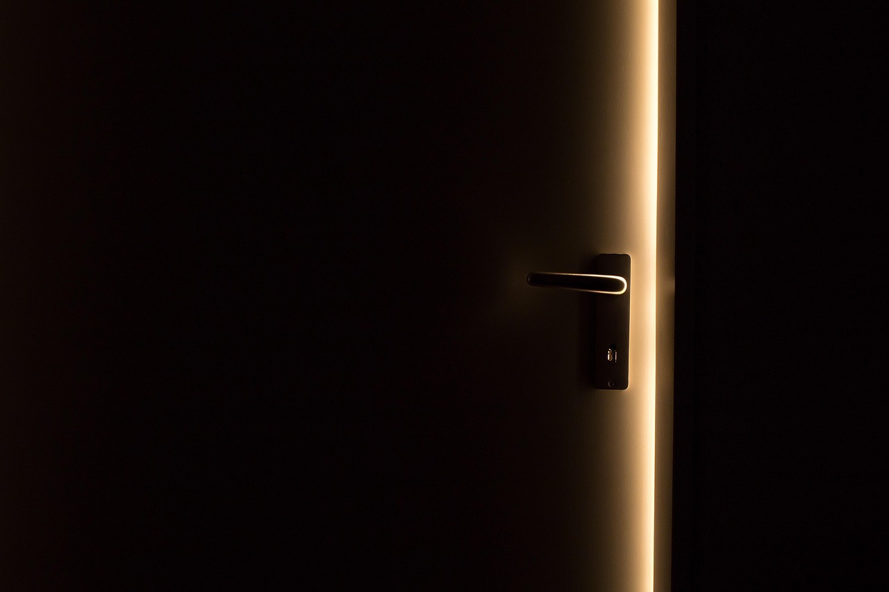 A dark door slightly open with warm light coming through