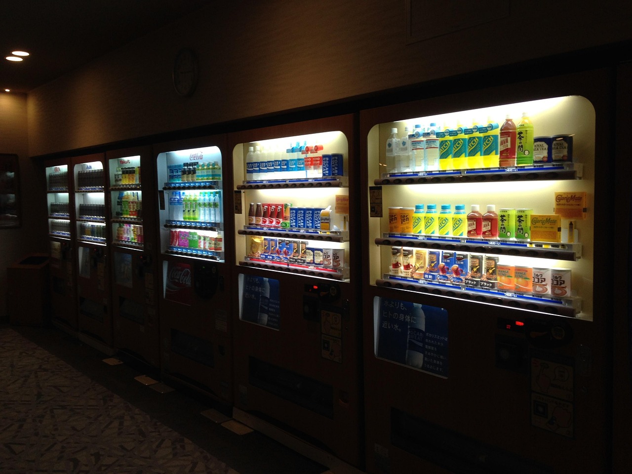A row of brightly lit vending machines in a dark room, representing quick fixes and short-term comfort.