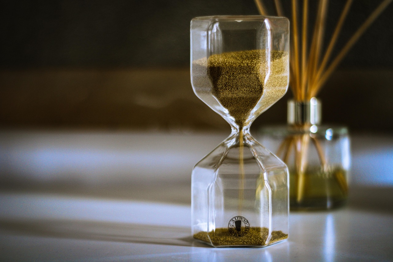 Golden sand falling through a glass hourglass, symbolising patience and waiting.