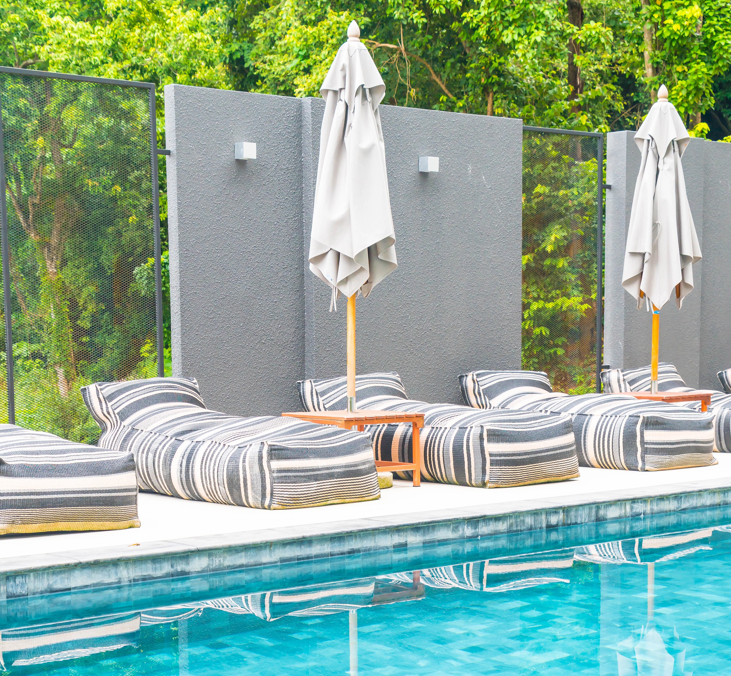 Modern outdoor lounge area with striped sunbeds and umbrellas beside a clear blue swimming pool after Mooresville Pool Renovation.