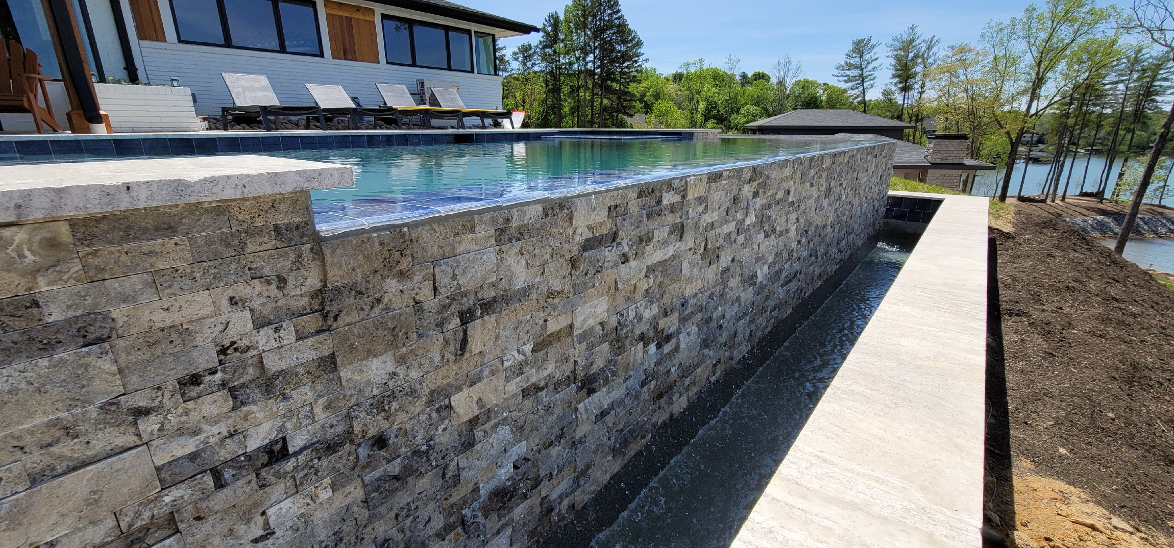 Luxury Mooresville above ground pool installation featuring a stone retaining wall, infinity-style design, and a scenic lakefront backyard view.