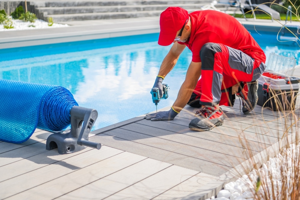 Mooresville swimming pool installers working on pool deck installation with tools and equipment beside a residential swimming pool.
