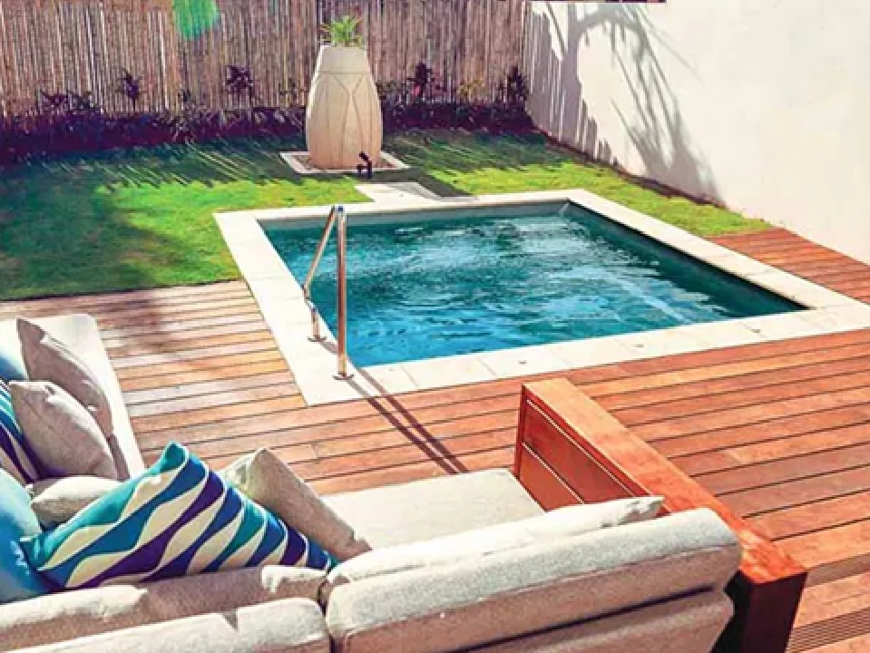 A small, square plunge pool is integrated into a wooden deck with comfortable outdoor seating. The background features a grass lawn and a bamboo fence. Focus keywords: Mooresville Build A Pool In My Backyard by Craft Master Pools and Spas.