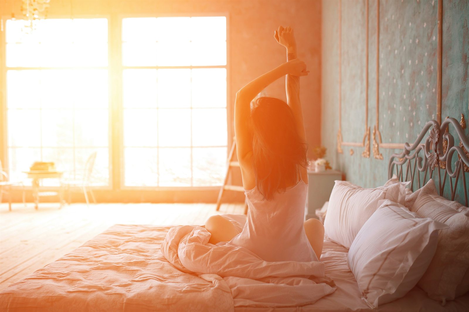 Femme s'étirant au réveil sur son lit dans une chambre baignée de lumière au lever du soleil