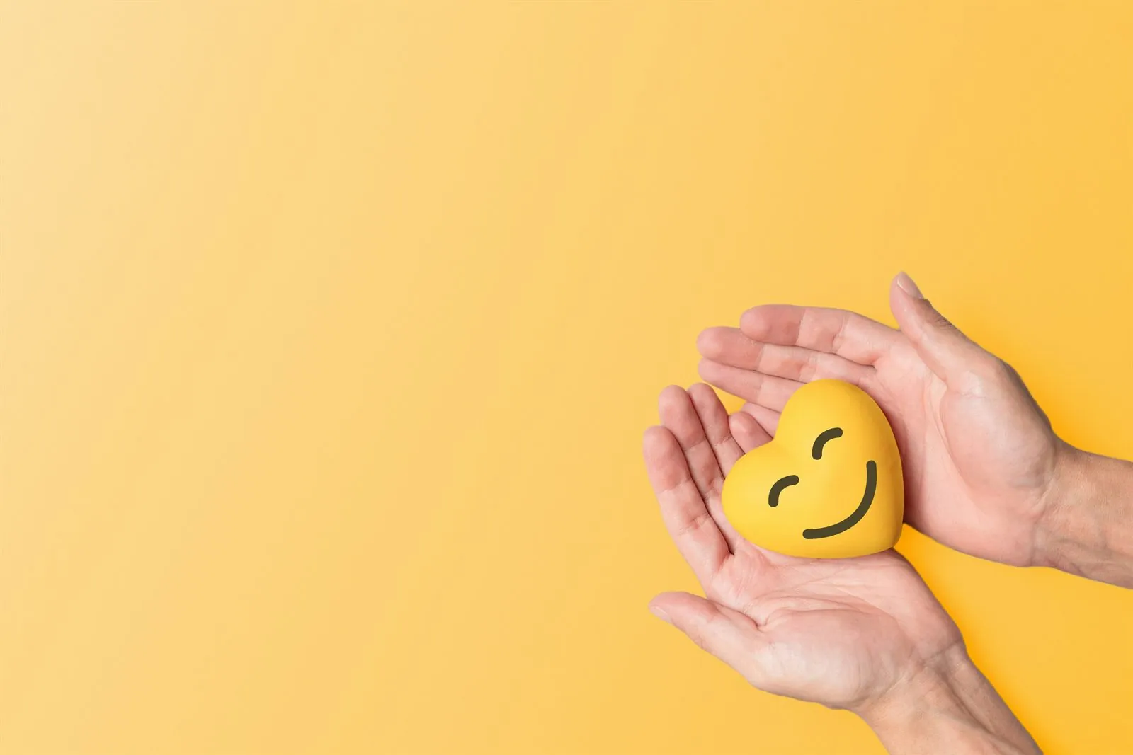 Deux mains tenant délicatement un cœur jaune souriant sur fond jaune