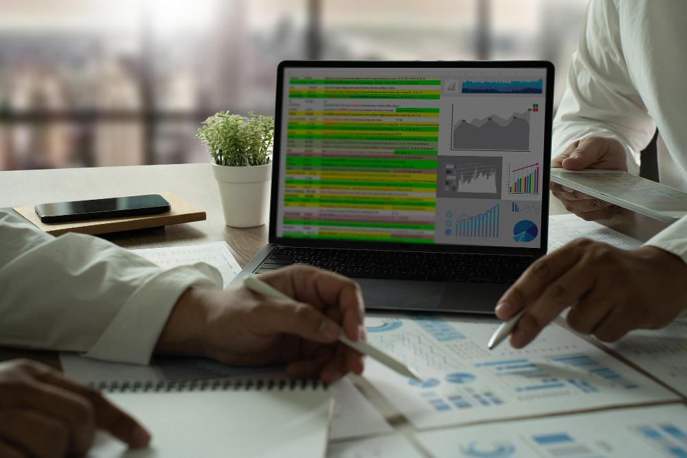 Two people sitting around a desk discussing data on a computer and sheets of paper