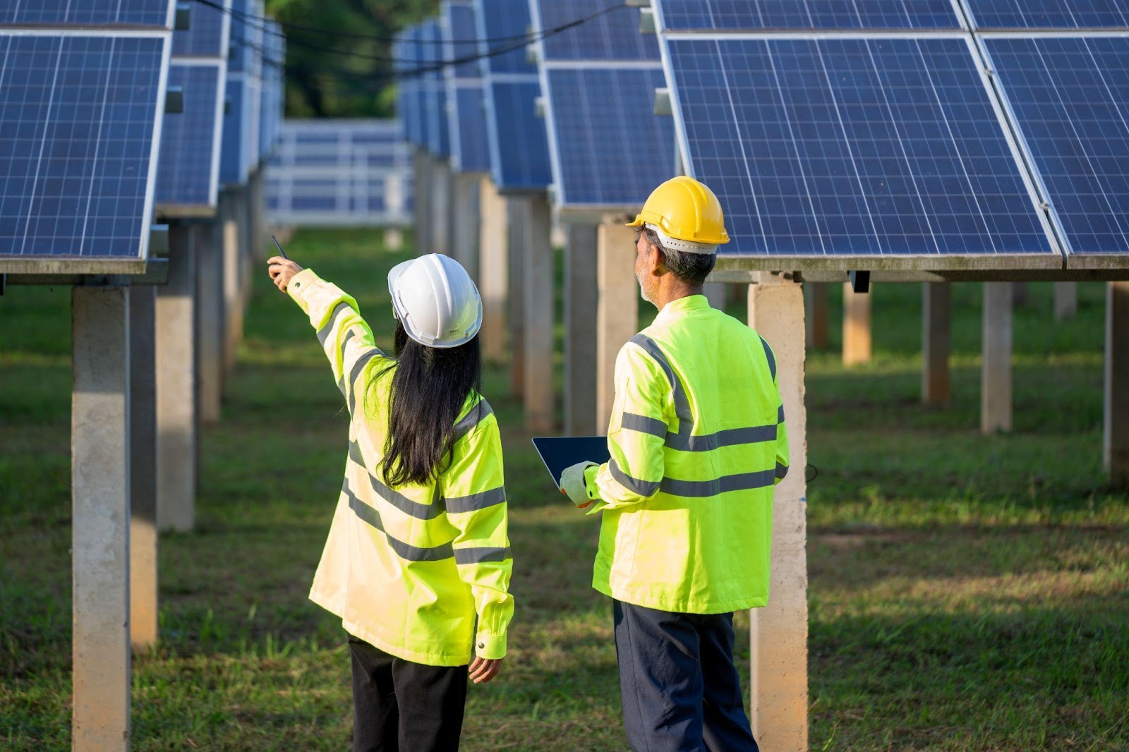 Two people dressed in protective gear are inspecting solar panels on the ground