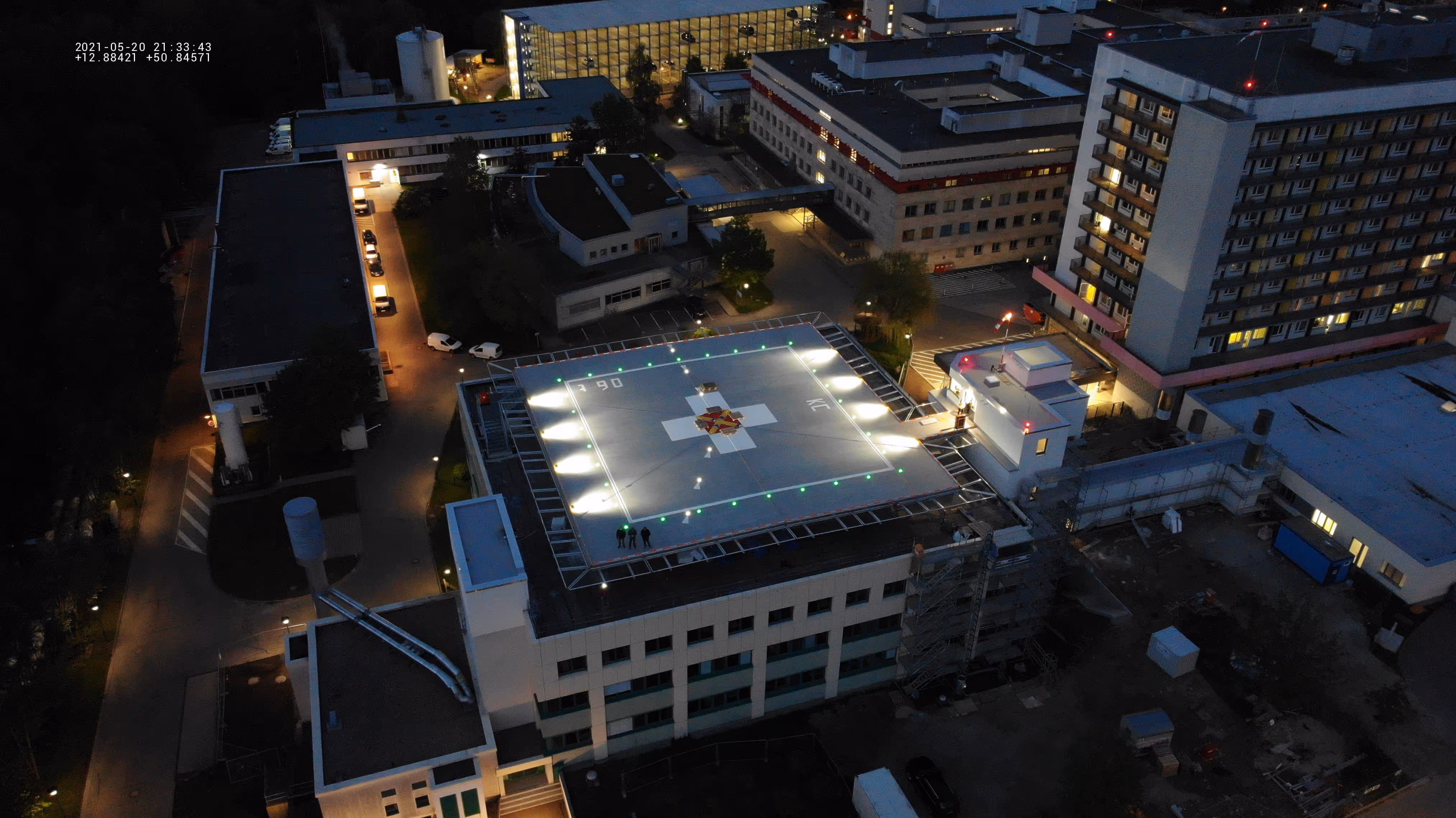 Luftaufnahme eines Krankenhauses bei Nacht mit beleuchtetem Hubschrauberlandeplatz auf dem Dach.