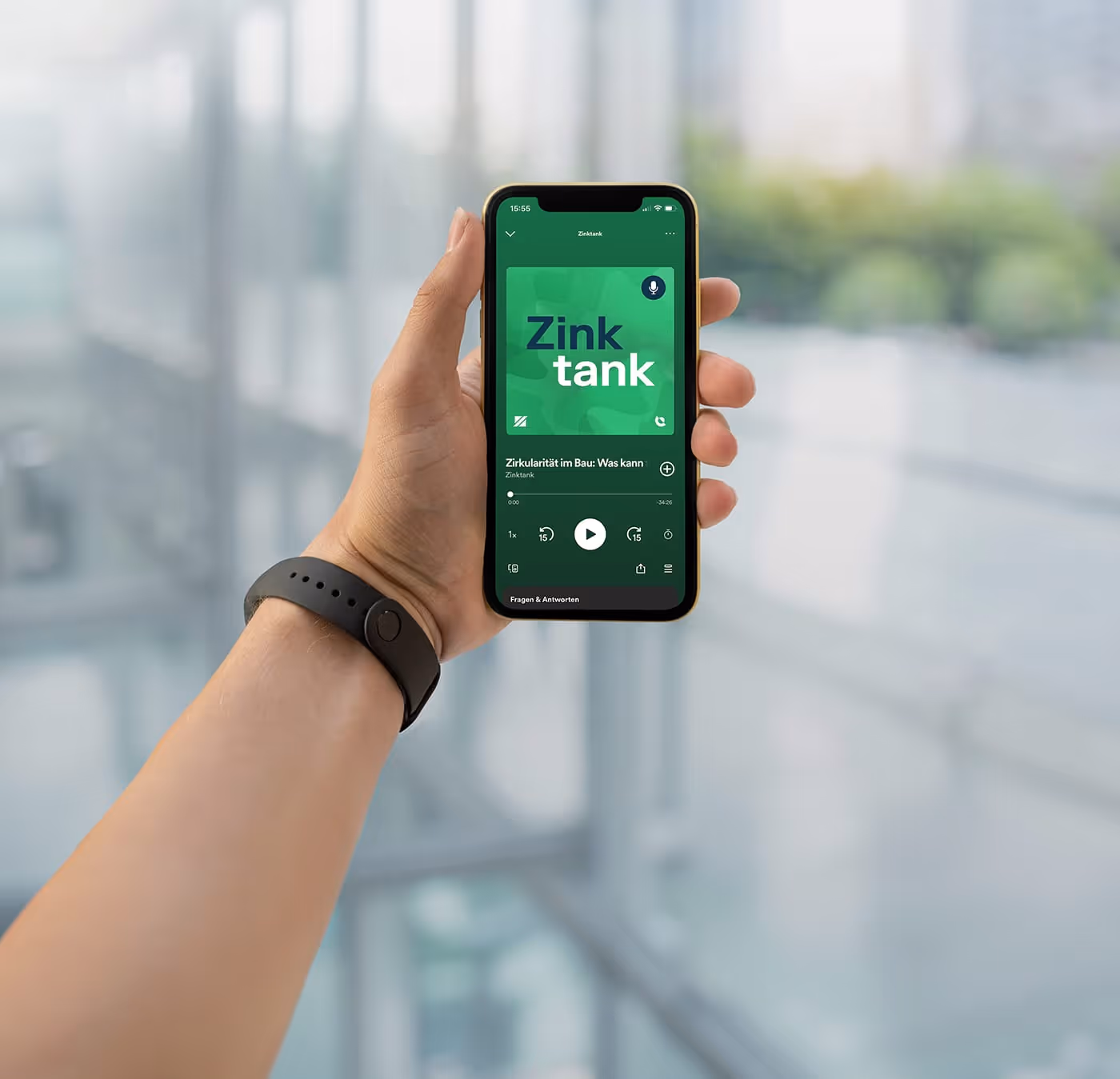 Hand hält ein Smartphone mit der Zinktank-Podcast-App, die eine Episode über Zirkularität im Bau abspielt.