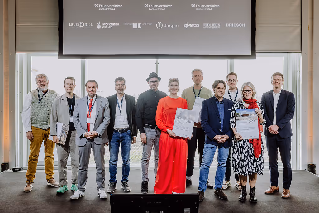 Elf Personen stehen nebeneinander auf einer Bühne, einige halten Urkunden, vor einer großen Projektionsfläche mit Firmennamen und Logos.