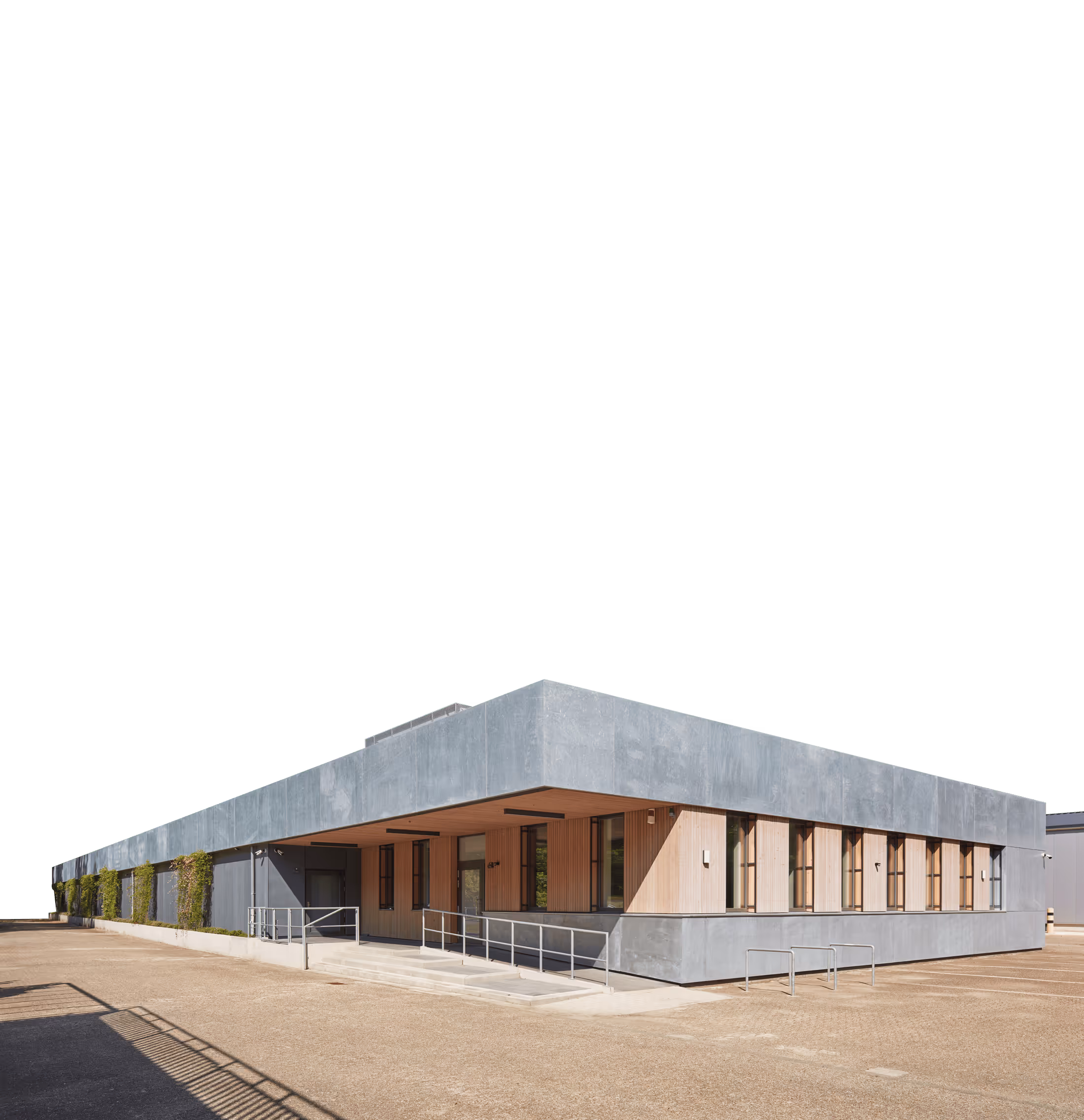 Modernes, flaches Gebäude mit Betonfassade und Holzverkleidungen an den Fenstern, umgeben von leerem Parkplatz.