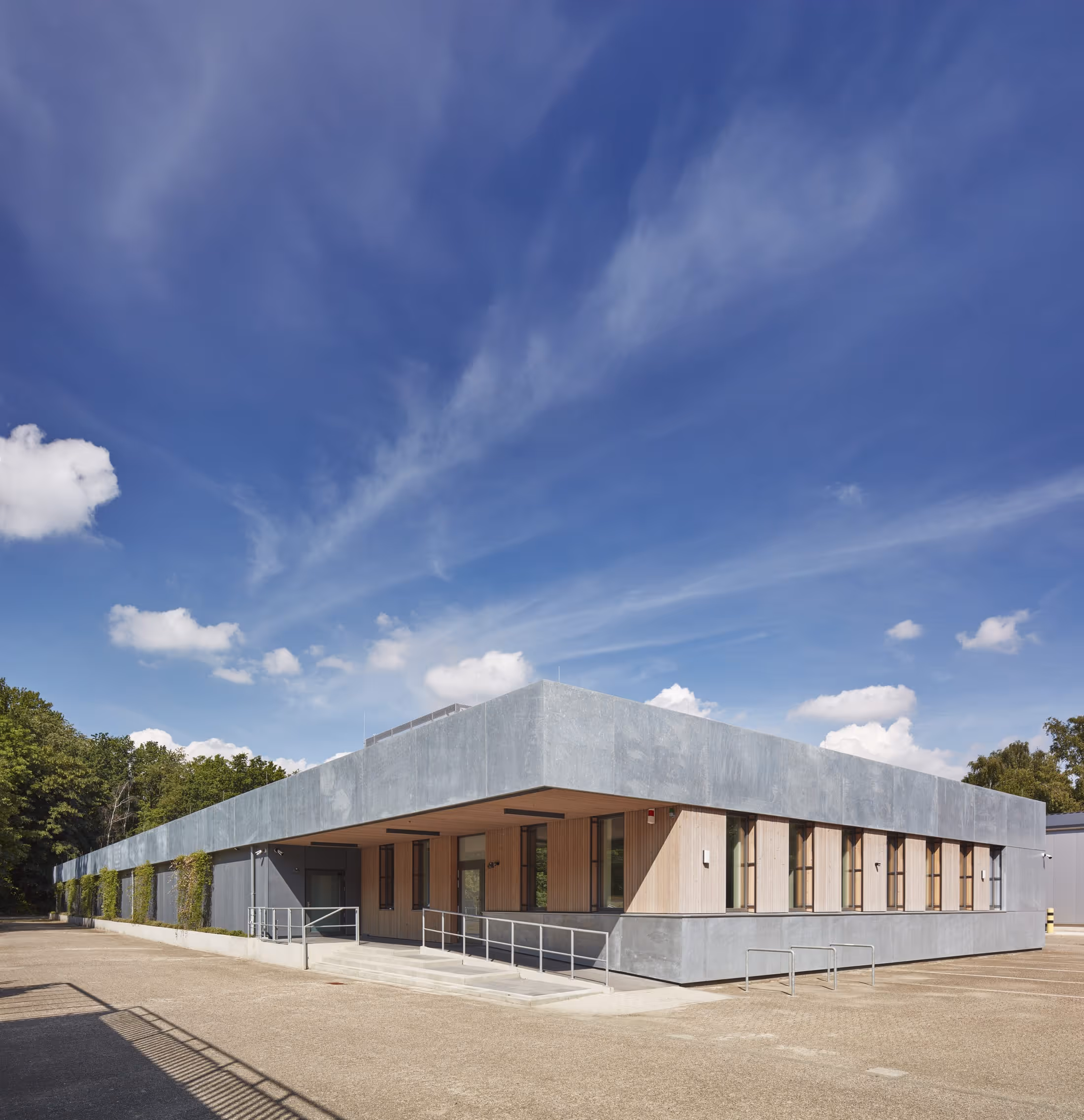Modernes Gebäude mit einer grauen Fassade und Holzverkleidung unter blauem Himmel mit weißen Wolken.