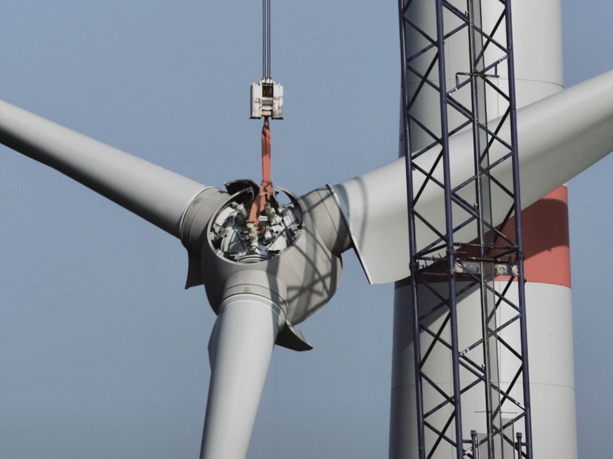 Nahaufnahme einer Windkraftanlage, bei der das Rotorblattgehäuse durch einen Kran für Wartungsarbeiten geöffnet wurde.