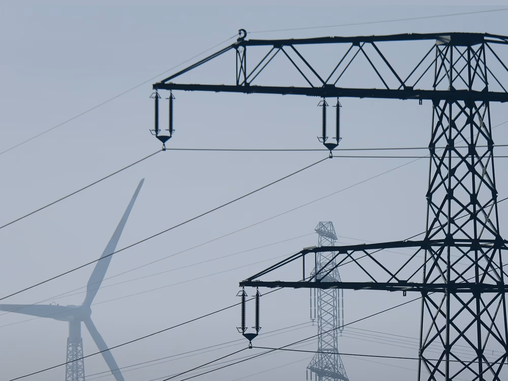 Strommasten und Windkraftanlage sind durch Nebel teilweise verdeckt sichtbar.