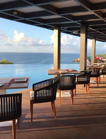 Beachfront restaurant with a wooden deck and set tables, offering breathtaking views of an infinity pool and the turquoise ocean. This Creole restaurant is located in a luxury hotel in Guadeloupe.