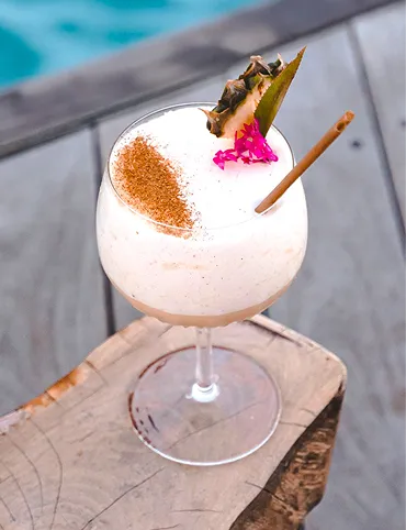 A clear cocktail with a white foam neck and a half-passion on top, placed on a golden platter. Typical of the drinks served in a luxury cocktail bar in Guadeloupe.
